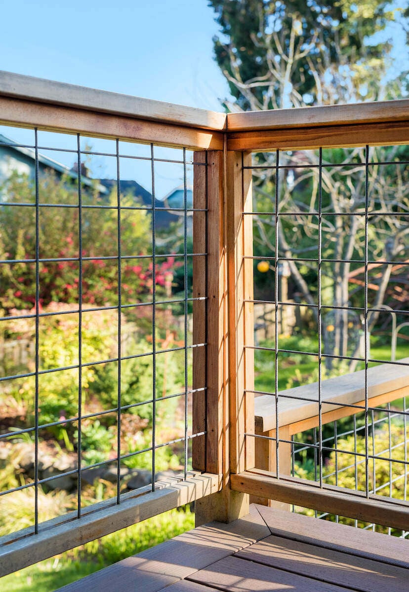 Close-up of a wooden deck corner with wire railing overlooking a lush backyard, designed by CB Construction in Seattle