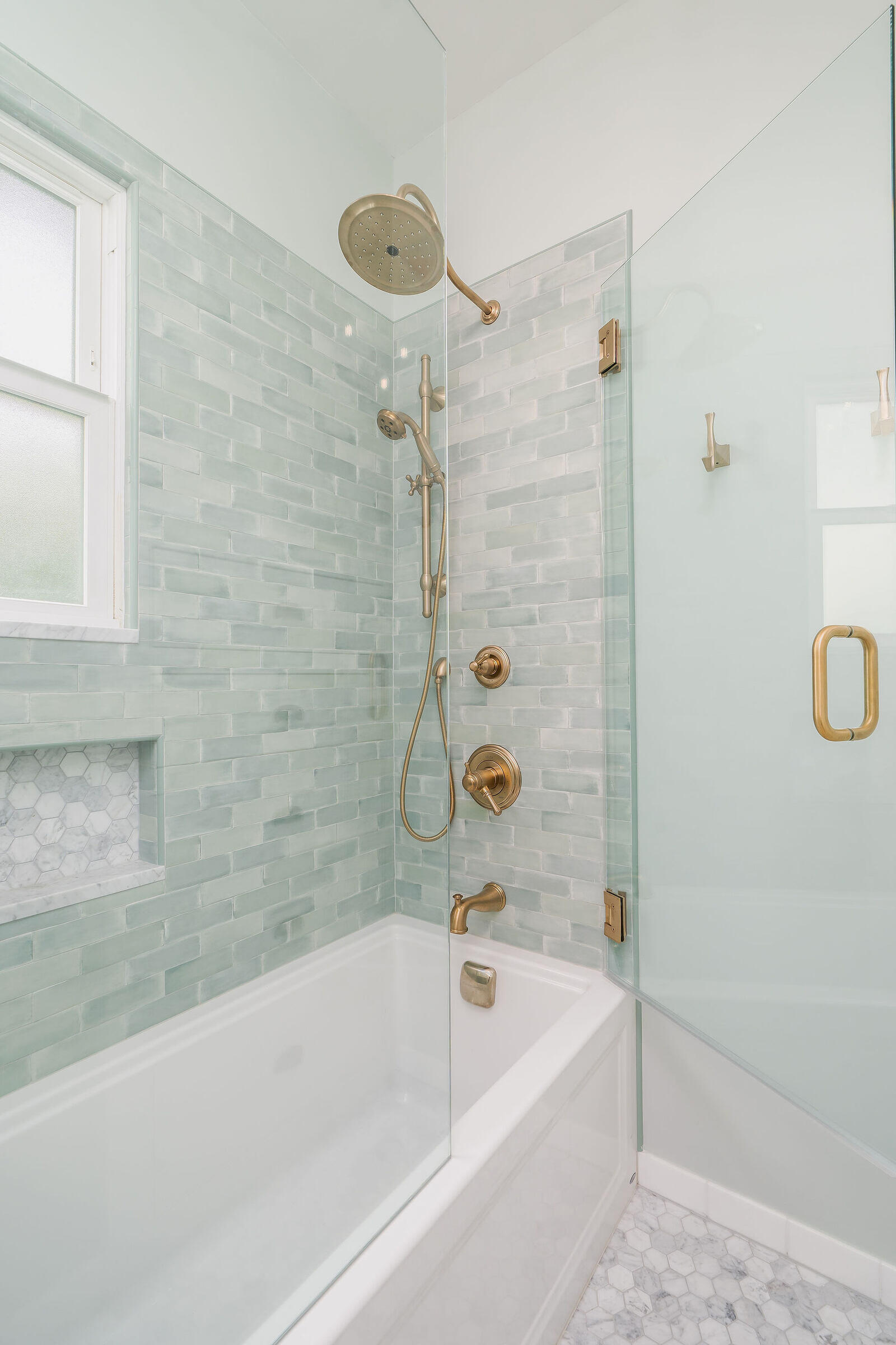 Glass shower with green subway tile and brass fixtures in a bathroom remodel by CB Construction, Seattle