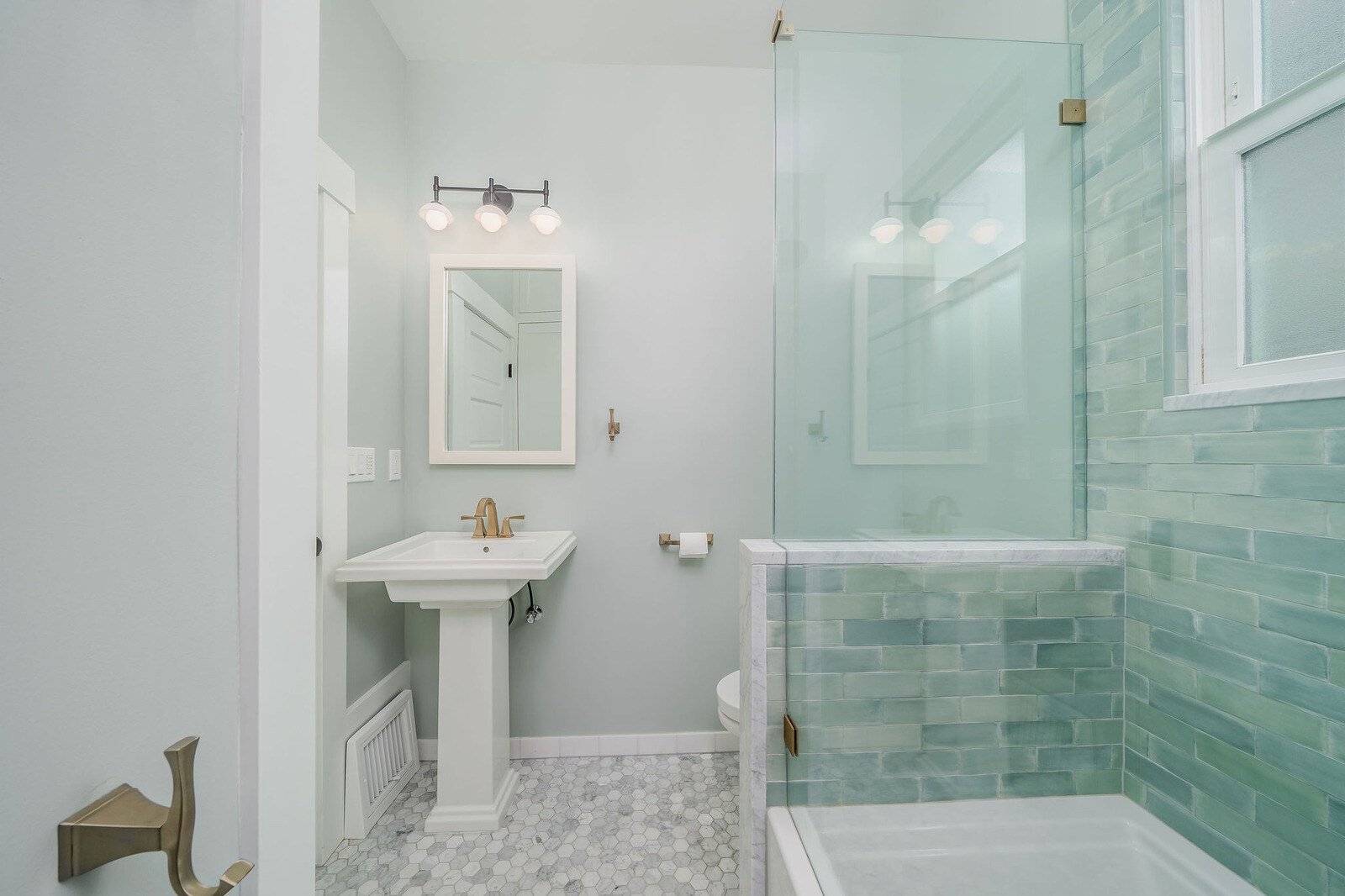 Shower detail with brass rain shower head and green tile in a remodeled Seattle bathroom by CB Construction